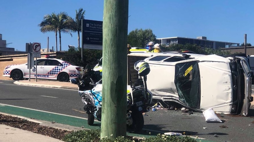 The damaged ute lies on its side with its windows smashed with police vehicles around it