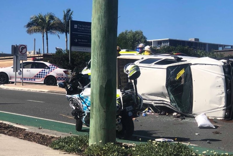 The damaged ute lies on its side with its windows smashed with police vehicles around it