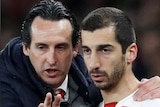 An Arsenal fan looks glum, the Europa League trophy stands on a pedastal, and Unai Emery gives directions to Henrikh Mkhitaryan