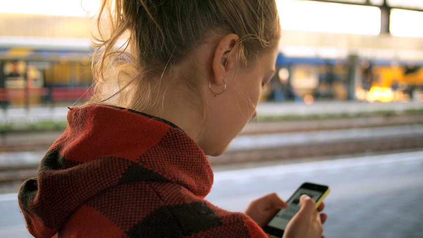 A woman stands on a train platform checking her phone.