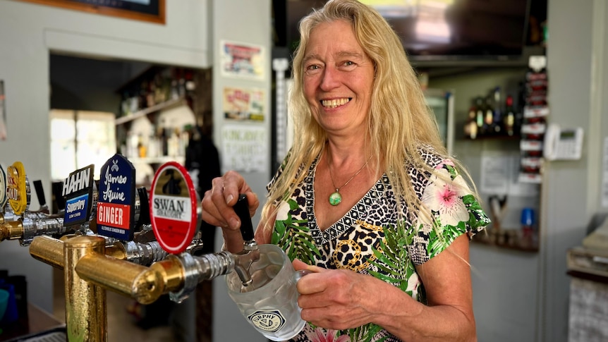 A woman with blonde hair pours a beer behind a bar