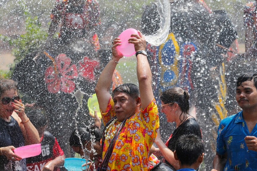 Man throws bowl of water up in the air as water sprays all around him in large crowd