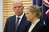 Peter Dutton watches Susan Ley speak at a lectern, her hands out as she gestures