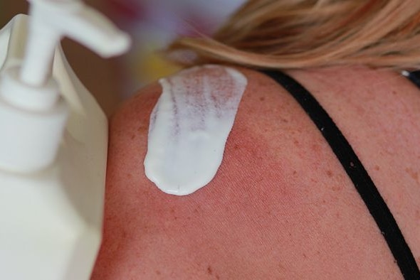 A woman applies a white liquid to her shoulder.