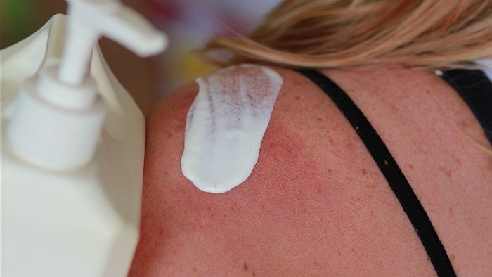 Close-up of a woman applying sunscreen to her shoulder.