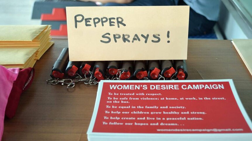 A sign reads 'pepper spray' with cannisters below and a leaflet on a women's rights campaign sits in the foreground of a table.