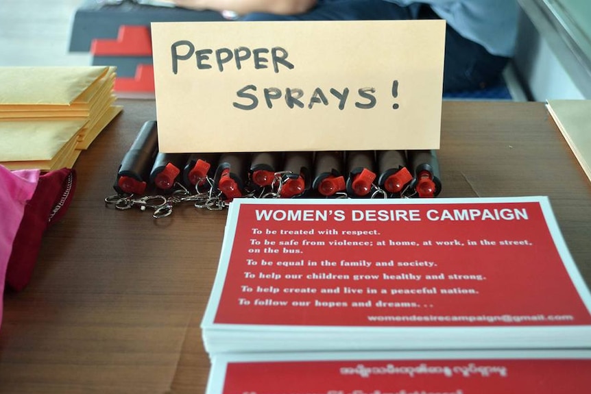 A sign reads 'pepper spray' with cannisters below and a leaflet on a women's rights campaign sits in the foreground of a table.