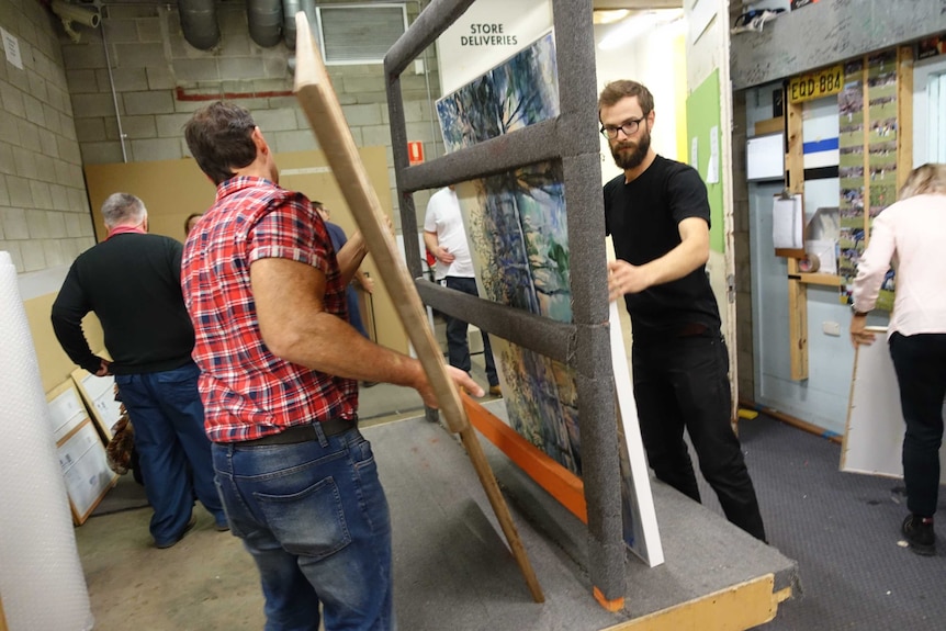 Two men loading paintings onto a trolley for the Archibald Prize.