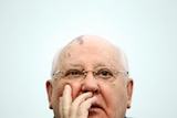Mikhail Gorbachev looks ahead while wearing glasses and with his hands on his face.