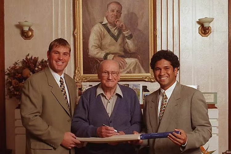Three men hold a bat together and pose for a photo.
