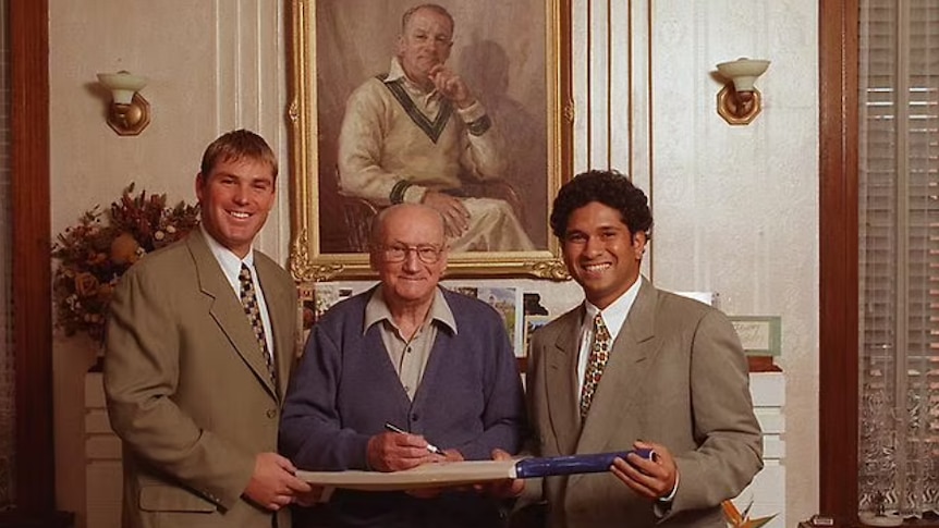 Three men hold a bat together and pose for a photo.
