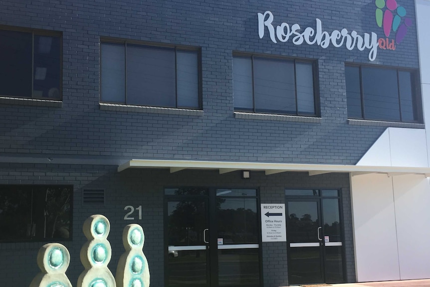 A black brick building with a "Roseberry Qld" sign. There is a white sign that points to reception.