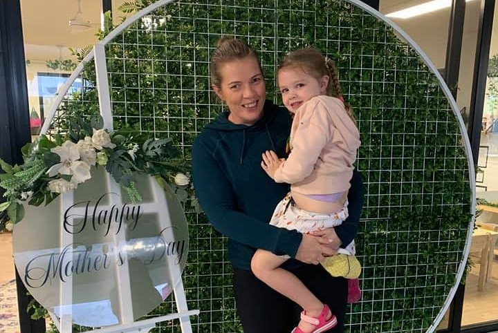 A woman in a green jumper stands with her daughter in her arms