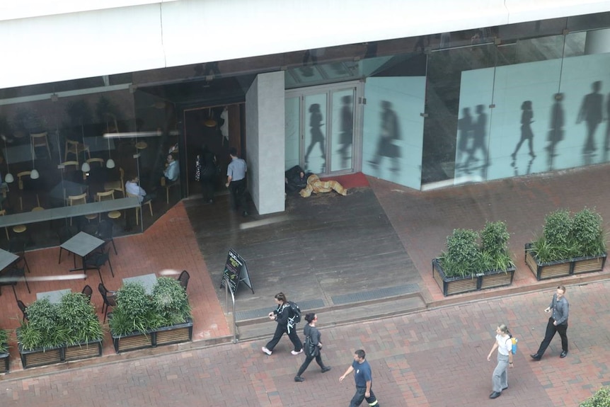 A homeless person lays on the ground with blankets near an Adelaide cafe in the CBD.