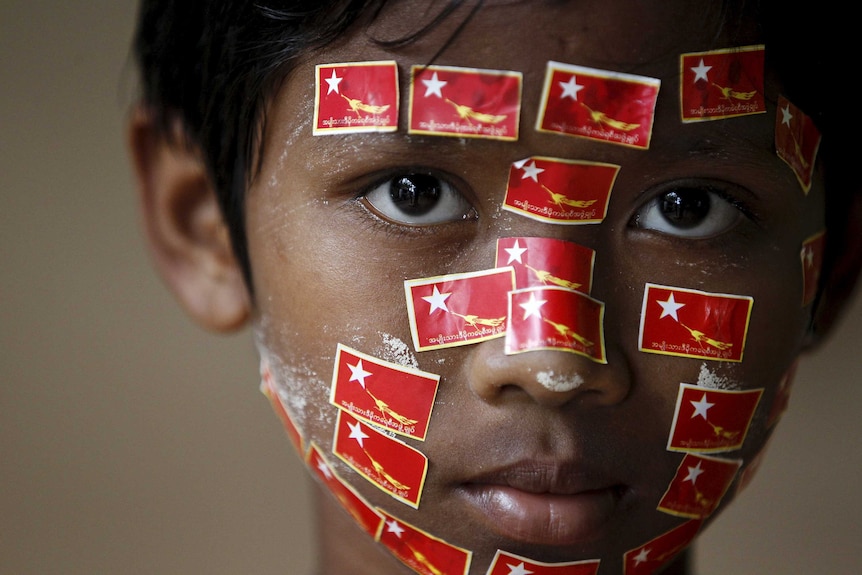 A boy places stickers with National League for Democracy (NLD) party logo on his face