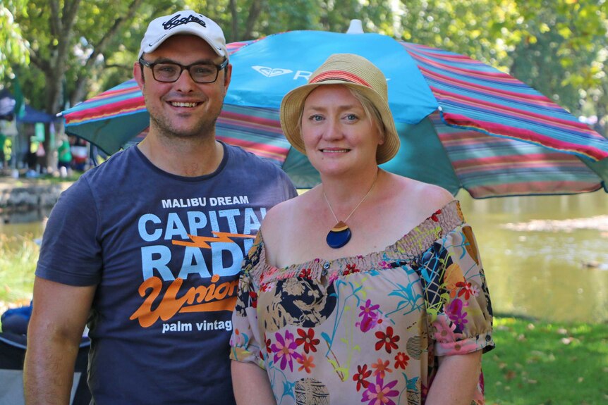 A man and a woman pose for a photo smiling in front of a large picnic umbrella.
