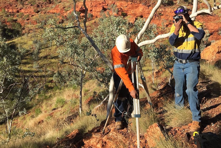 2 men in front of a tree with survey equipment.