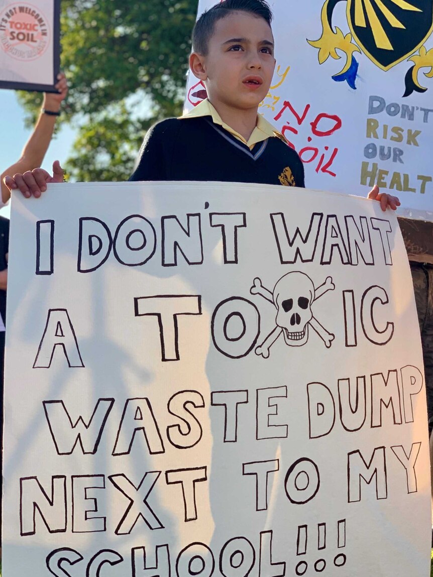 A boy with a sign that says I don't want a toxic waste dump next to my school.
