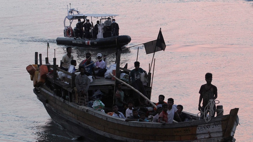 Rohingya refugees sit on a boat on the water at dusk.