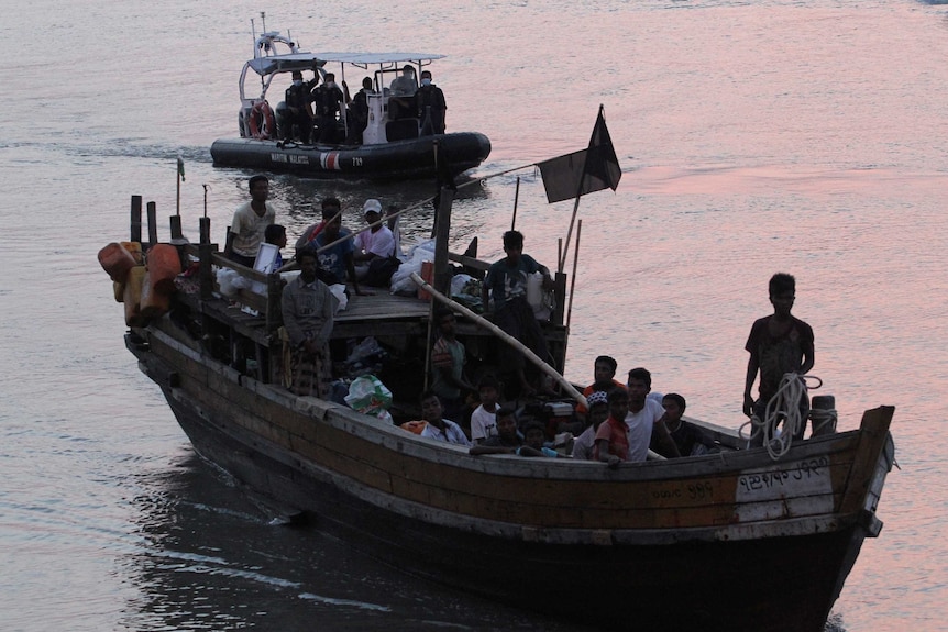 Rohingya refugees sit on a boat on the water at dusk.