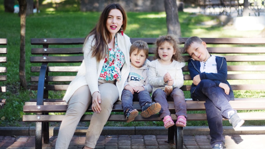 a woman sits on a park bench with two young twins and a slightly older boy