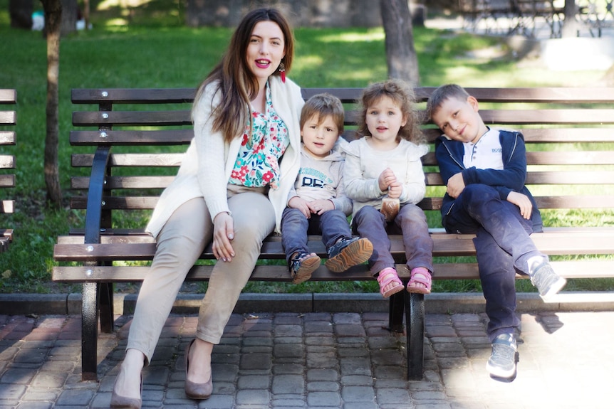 a woman sits on a park bench with two young twins and a slightly older boy