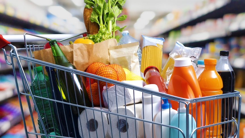 A picture of a shopping trolley with different grocery items with a blurry background of a shopping aisle