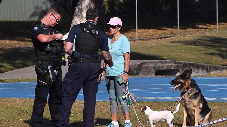 Police speak with a woman walking her dogs at a crime scene in Frascott Park,