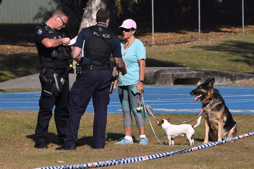 Police speak with a woman walking her dogs at a crime scene in Frascott Park,