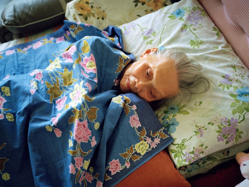 Old woman lying in bed with floral sheets and pillowcase