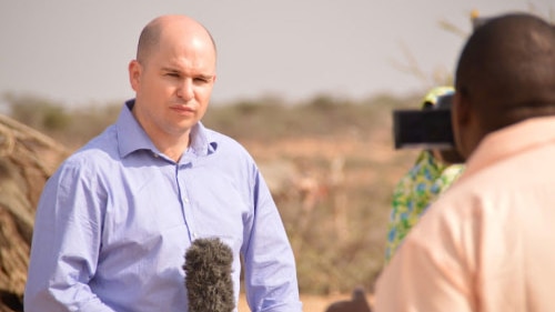 Martin Cuddihy stares at a handheld camera, with the desert in the background.