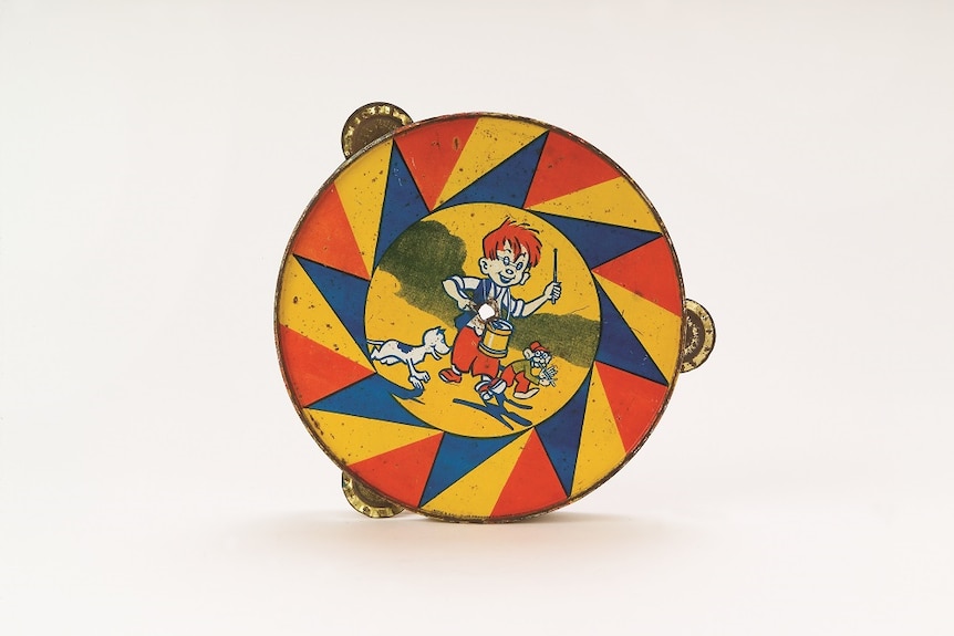 A vintage toy tambourine with an illustration of a child banging a drum, a monkey playing flute and a dog chasing