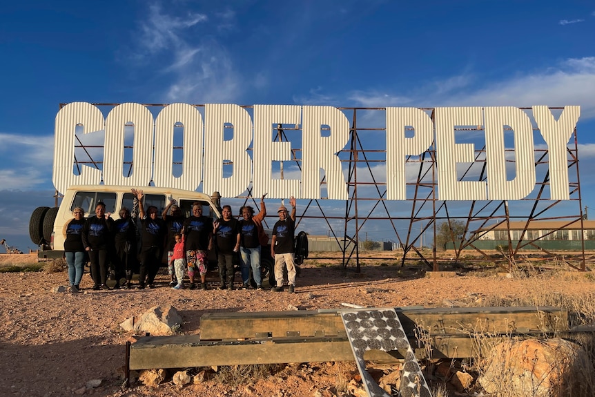 people stand in front of large Coober Pedy sign
