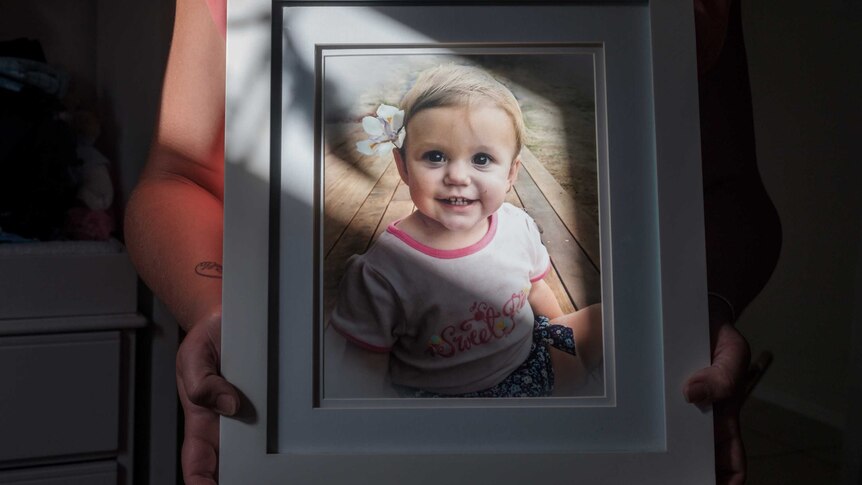 A framed photo of a toddler wearing a pink top and a flower in her left ear