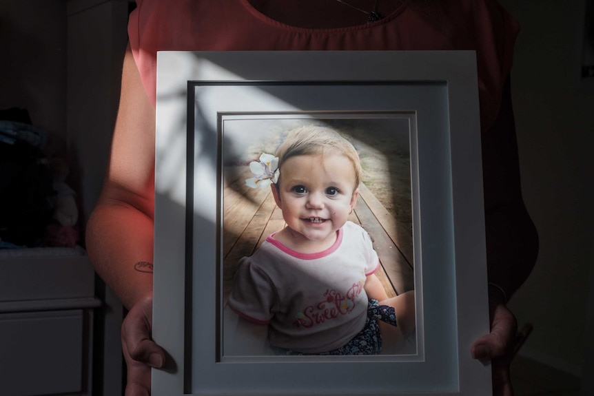 A framed photo of a toddler wearing a pink top and a flower in her left ear