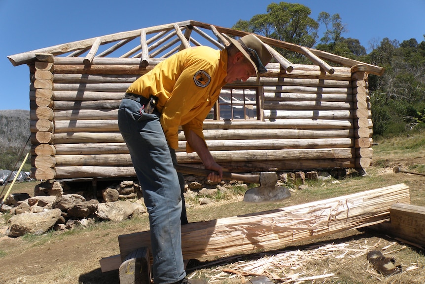 A man chopping wood outside a log cabin.