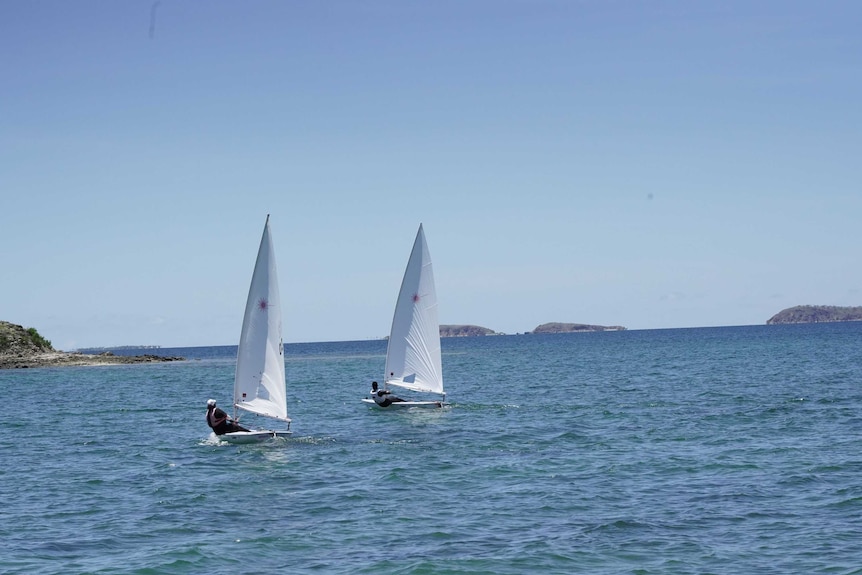 Two people on two boats sail on water with a clear sky above them.