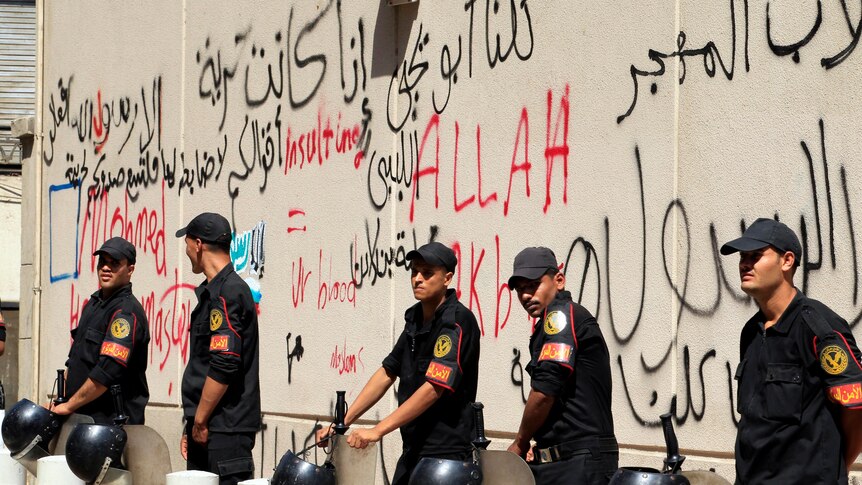 Security personnel stand guard near a wall with graffiti at the US embassy in Cairo.