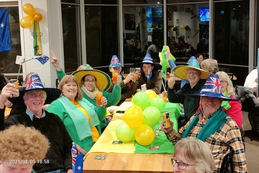 Happy people in green and gold with coloured balloons in a restaurant cheering
