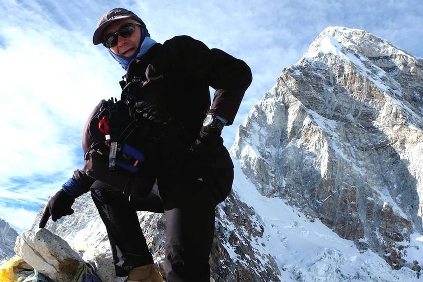 A man in hiking gear poses for a photo at the top of a snowy peak