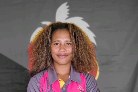 Front-on portrait of a female cricketer from Papua New Guinea. She has a broad smile and very curly brown hair.
