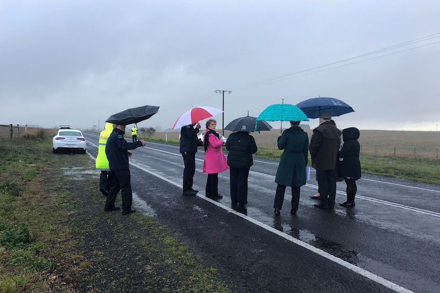 A group of people in coats with umbrellas stand on a highway