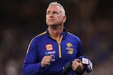 A mid-shot of West Coast Eagles coach Adam Simpson on ground with a blue and yellow team jumper on, looking upwards.