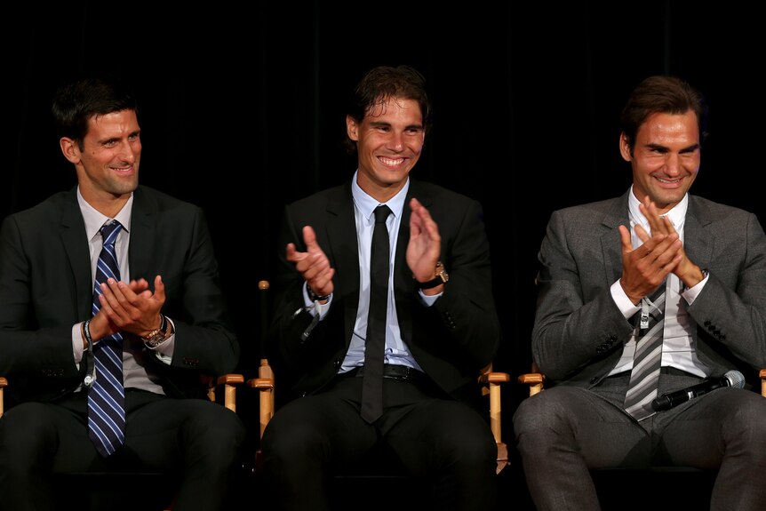 Novak Djokovic, Rafael Nadal and Roger Federer sit on stage in suits, applauding.