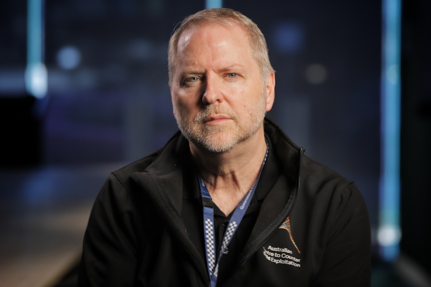 Man wearing a black jacket and blue lanyard.