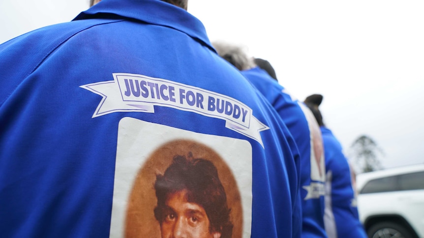 A relative of deceased Indigenous teenager Lewis "Buddy" Kelly wears a blue footy shirt with the 16-year-old's face on the back.