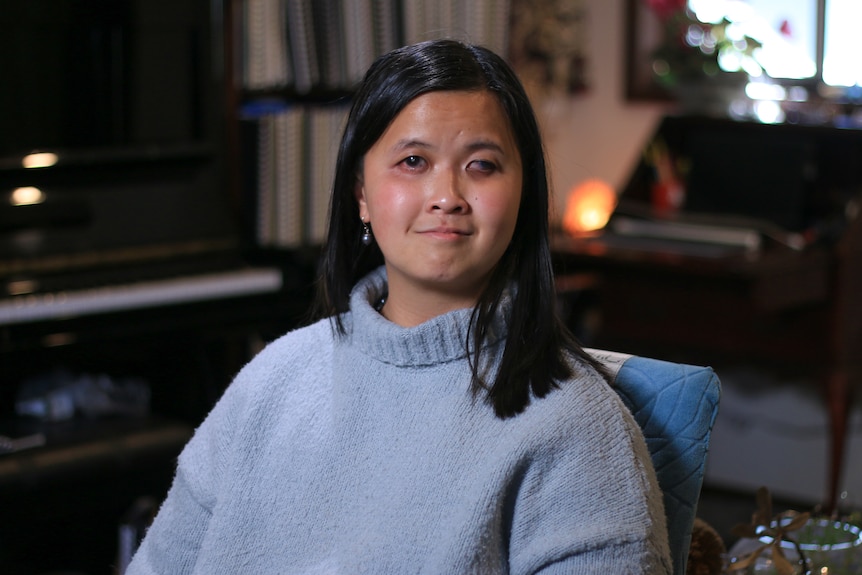 Ria Andriani wears a pale blue jumper, facing the camera in a portrait taken inside her home.