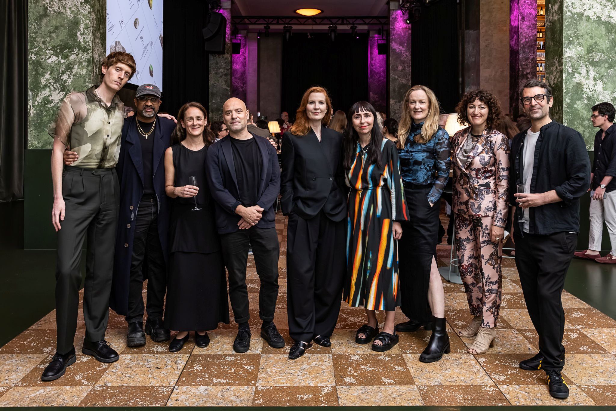 Um grupo de nove pessoas reunidas em um evento em uma sala com piso de mármore