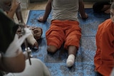 A man whose legs have been amputated sits on a prison floor.
