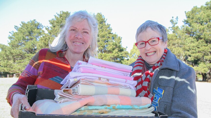 Two women hold a box of blanket pouches for baby wildlife.